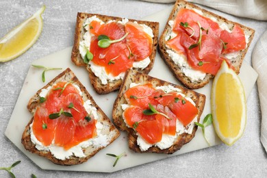 Photo of Delicious sandwiches with cream cheese, salmon and microgreens on light grey table, flat lay