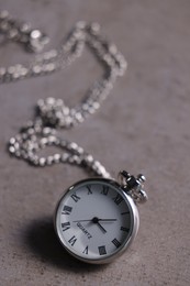 Photo of Silver pocket clock with chain on grey textured table, closeup