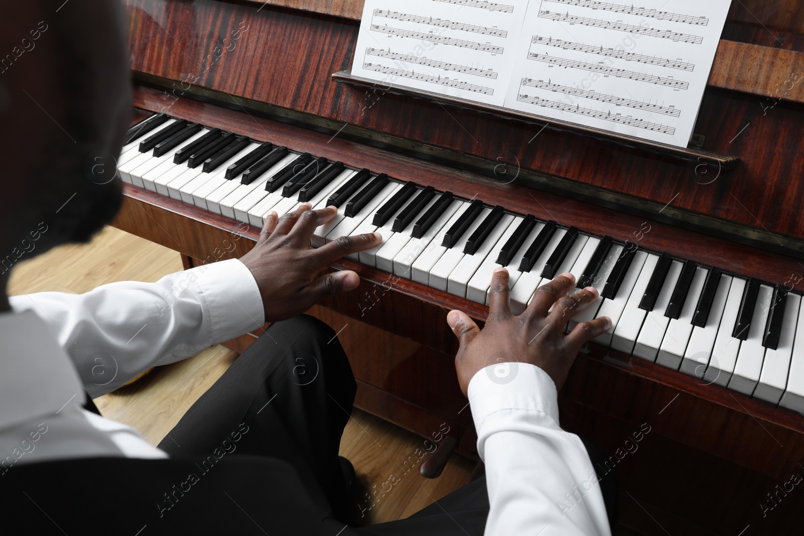 Photo of African-American man playing piano indoors, closeup. Talented musician