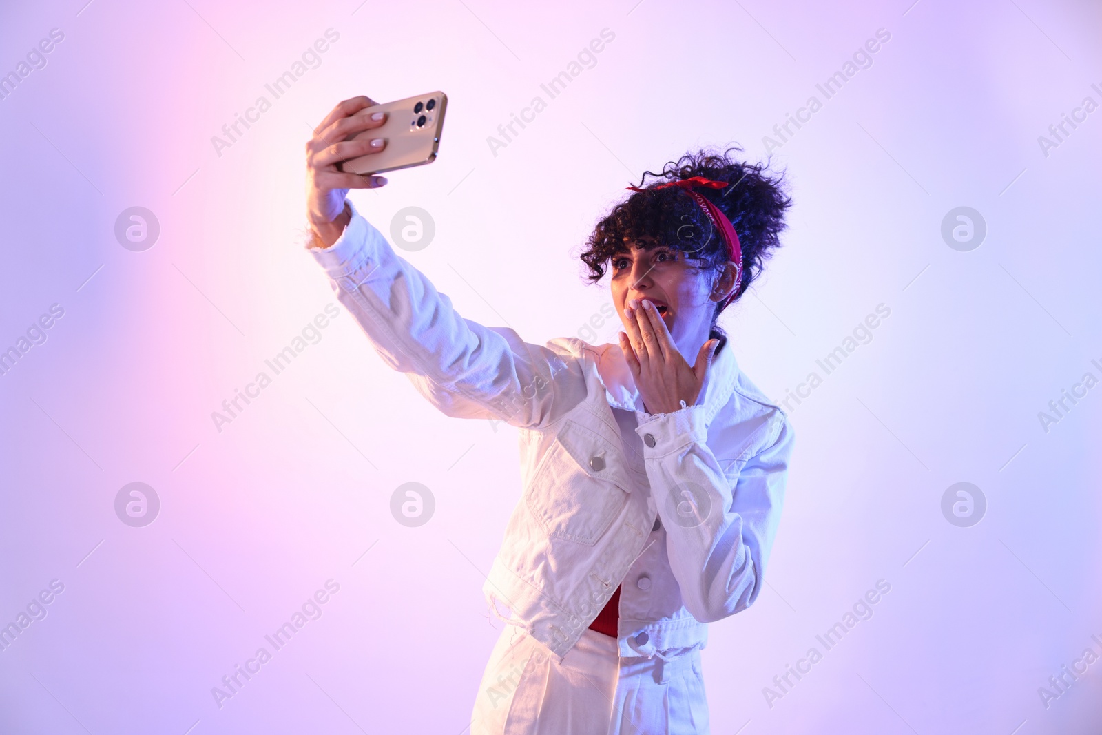 Photo of Beautiful young woman taking selfie on color background in neon lights