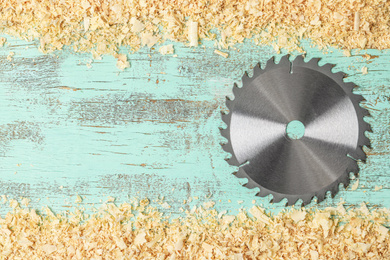 Photo of Saw disk and shavings on blue wooden background, flat lay with space for text. Carpenter's tool
