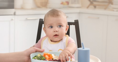 Mother feeding her cute little baby in kitchen