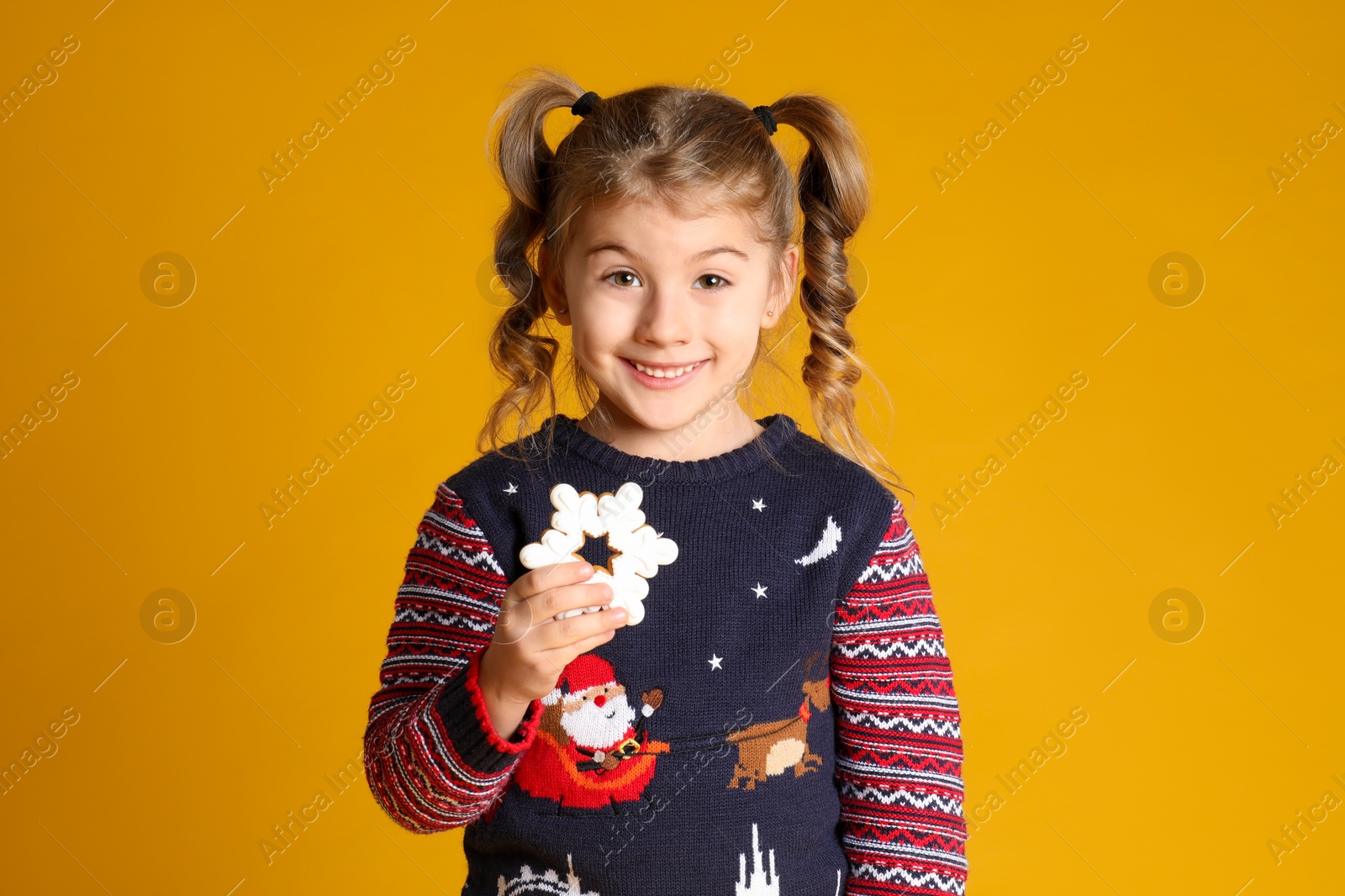 Photo of Cute little girl with Christmas gingerbread cookie on yellow background