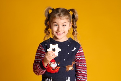 Cute little girl with Christmas gingerbread cookie on yellow background