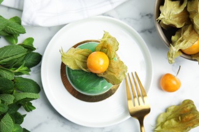 Delicious mousse cake decorated with physalis fruit on white marble table, flat lay