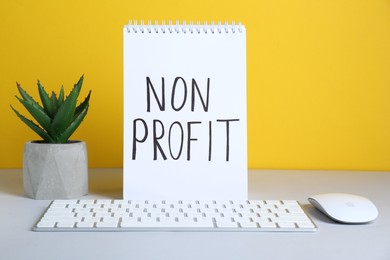 Photo of Notebook with phrase Non Profit, keyboard and houseplant on white table