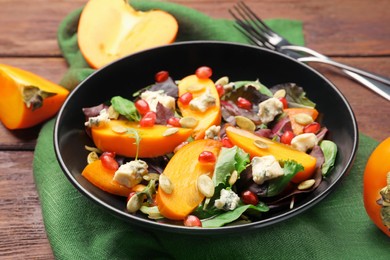 Delicious persimmon salad with pomegranate and spinach on wooden table, closeup