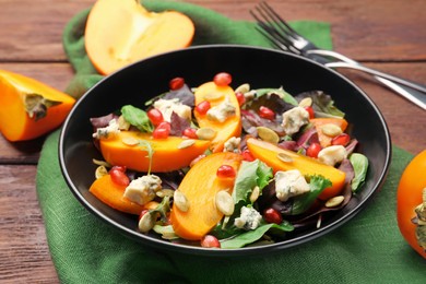 Photo of Delicious persimmon salad with pomegranate and spinach on wooden table, closeup