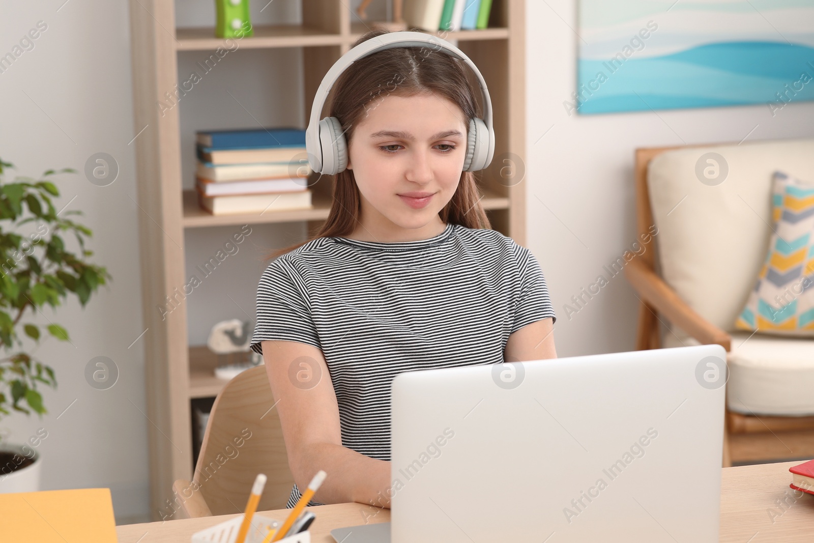 Photo of Cute girl using laptop and headphones at desk in room. Home workplace