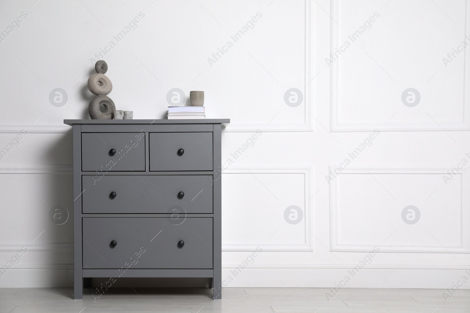 Photo of Different accessories on grey chest of drawers near white wall indoors