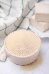 Photo of Granulated yeast in bowl on white tiled table, closeup