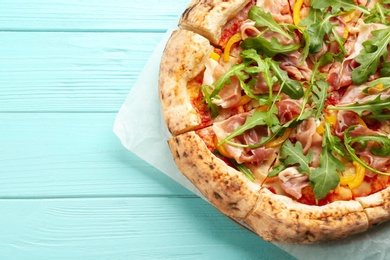 Tasty pizza with meat and arugula on light blue wooden table, top view. Space for text