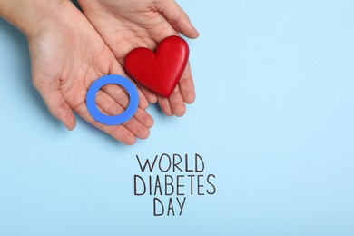 Photo of Woman holding blue paper circle and red heart near text World Diabetes Day on color background, top view