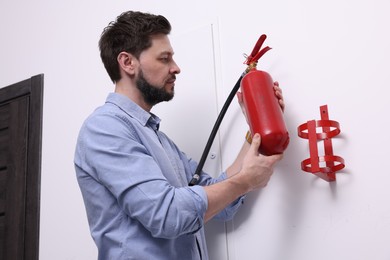 Photo of Man with fire extinguisher near white wall indoors