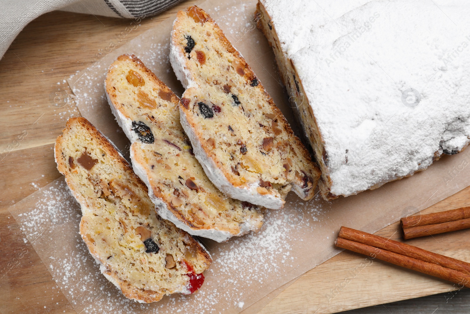 Photo of Traditional Christmas Stollen with icing sugar on wooden board, top view