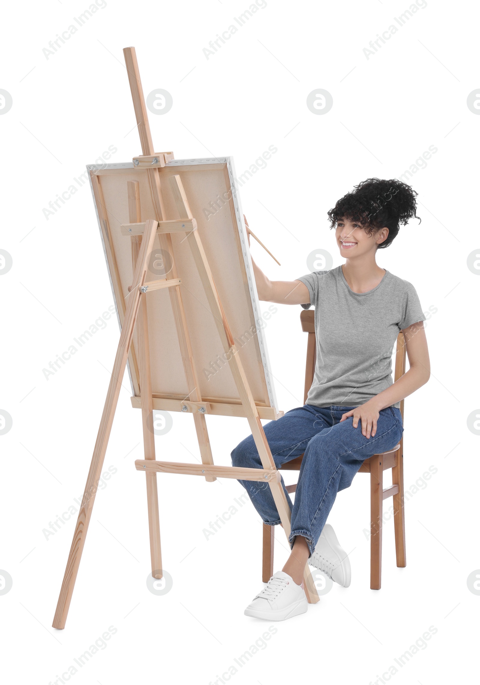 Photo of Young woman painting on easel with canvas against white background