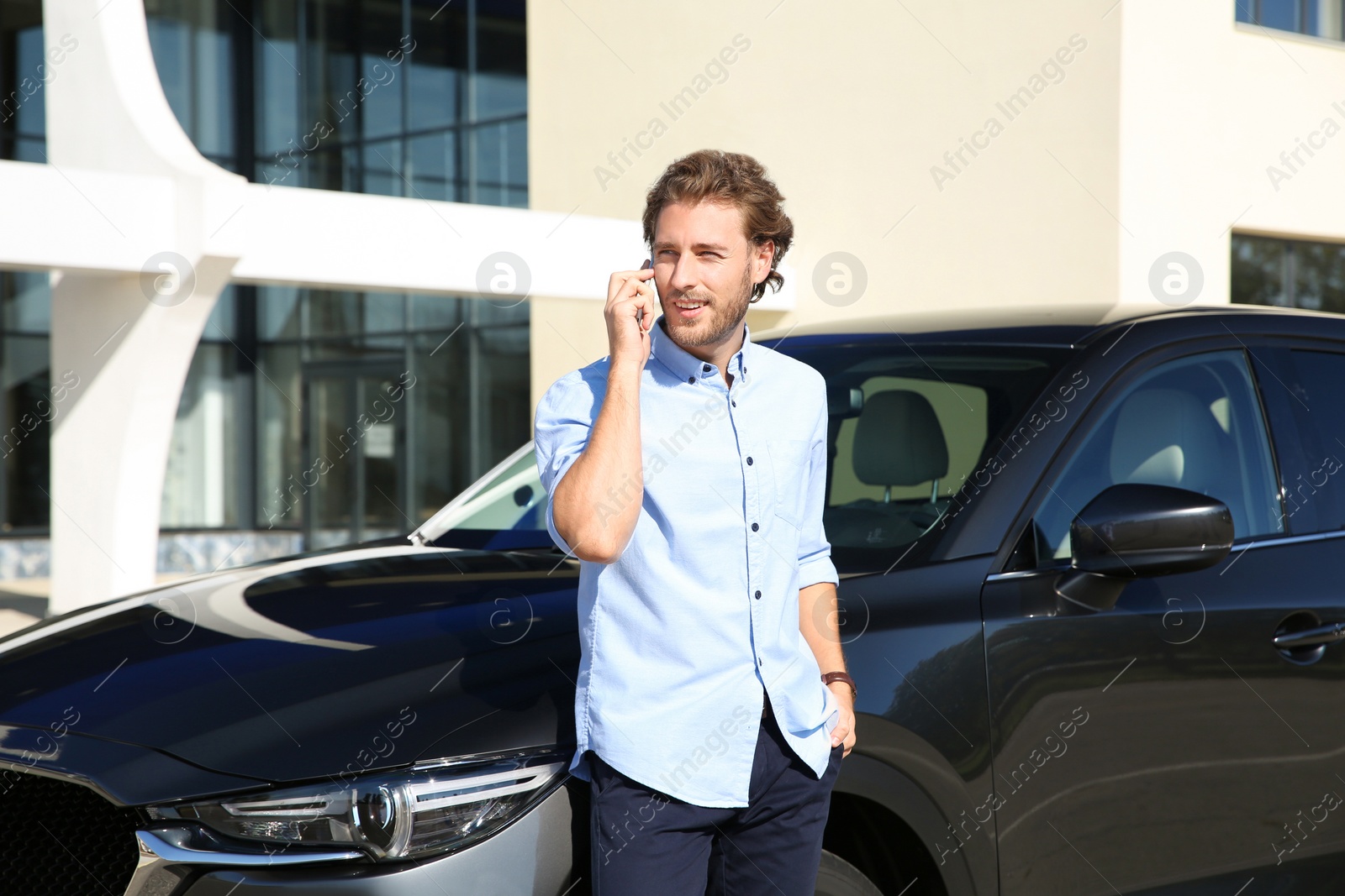 Photo of Young man talking on phone near modern car, outdoors