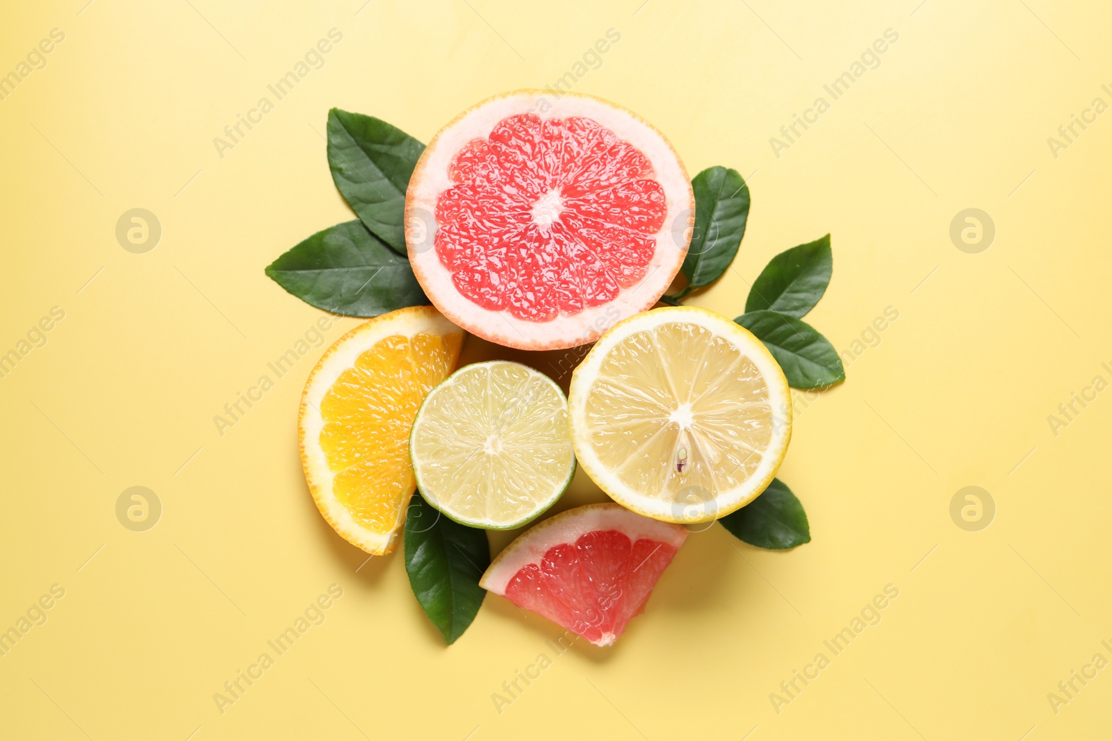 Photo of Different cut citrus fruits and leaves on yellow table, flat lay