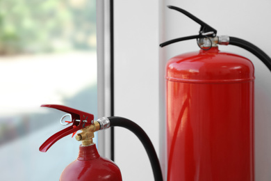 Photo of Different fire extinguishers near window indoors, closeup