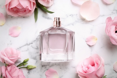 Photo of Bottle of perfume, beautiful flowers and petals on white marble table, flat lay
