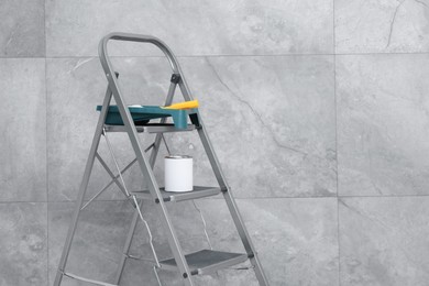 Photo of Metallic folding ladder and painting tools near grey wall, space for text