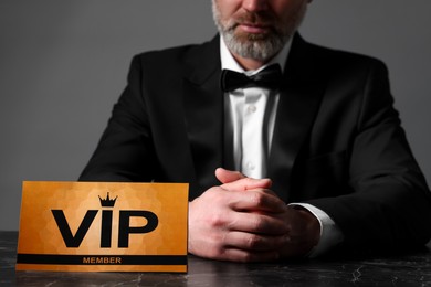 Man sitting at table with VIP sign on grey background, closeup