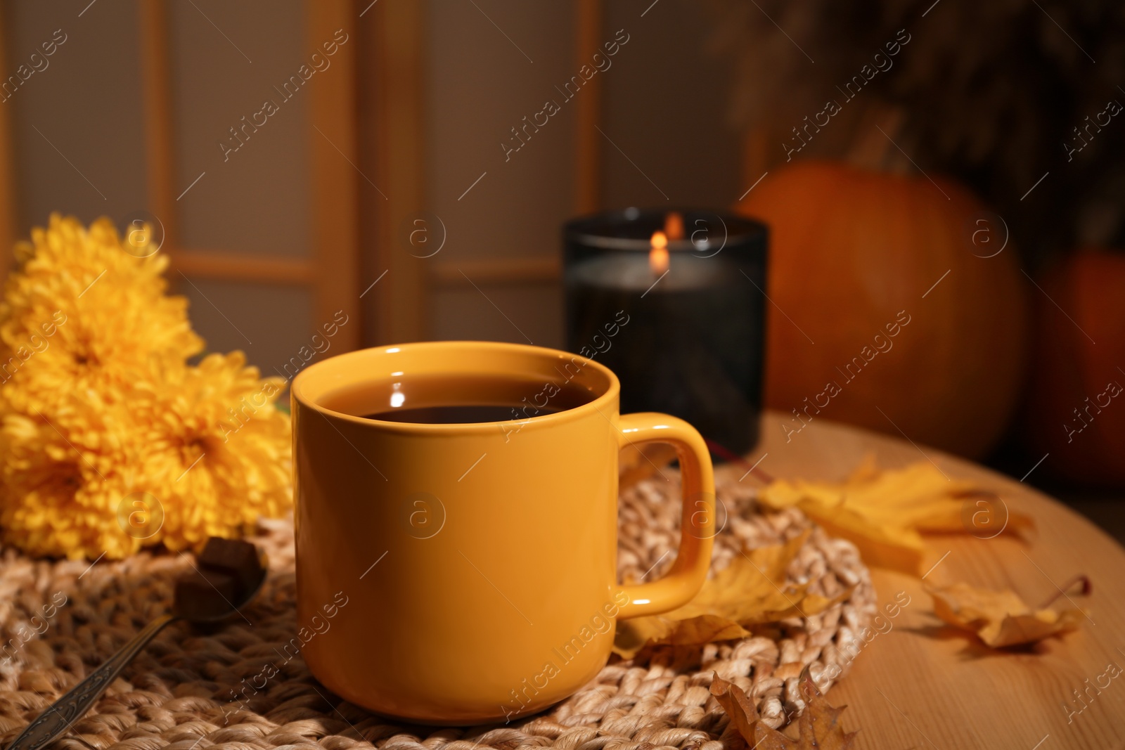 Photo of Cup of aromatic tea, beautiful flowers, candle and autumn leaves on wooden table indoors. space for text