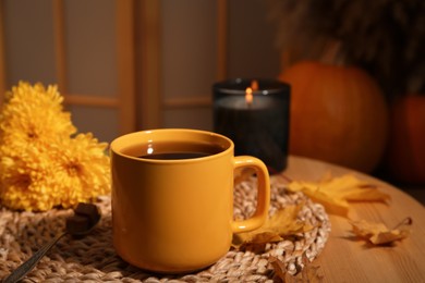 Photo of Cup of aromatic tea, beautiful flowers, candle and autumn leaves on wooden table indoors. space for text
