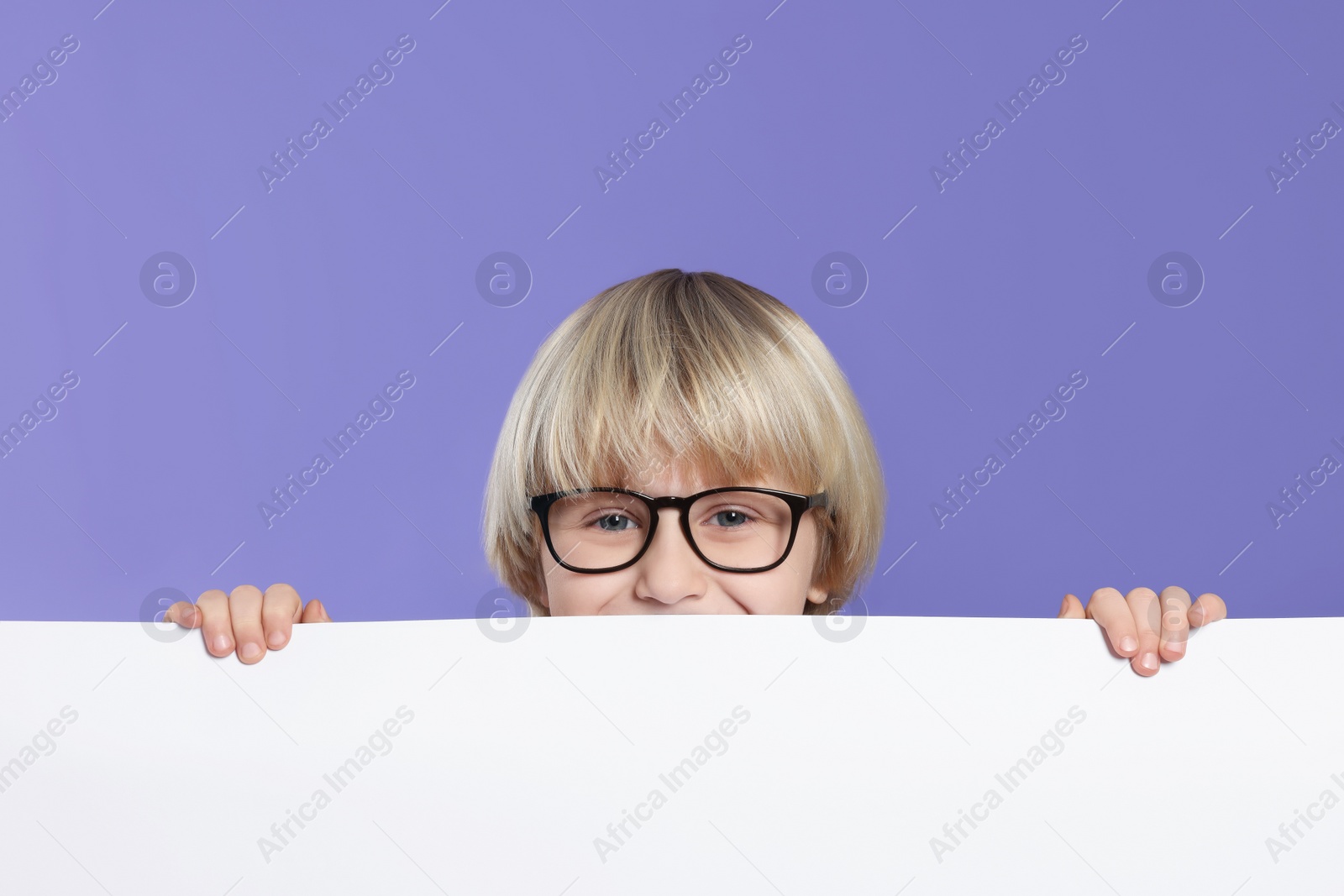 Photo of Cute little boy in glasses with blank board on purple background
