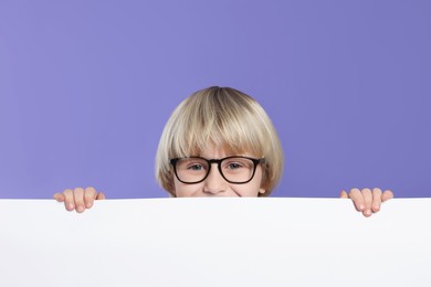 Photo of Cute little boy in glasses with blank board on purple background