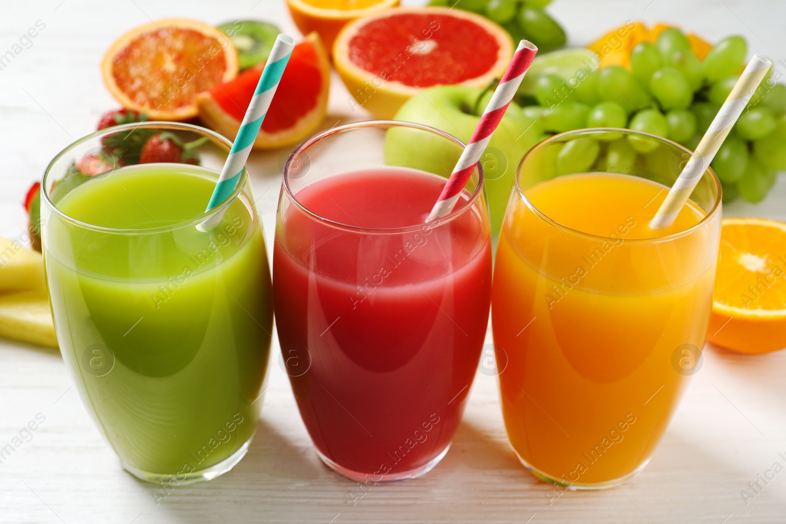 Photo of Glasses of different juices with straws and fresh fruits on wooden table