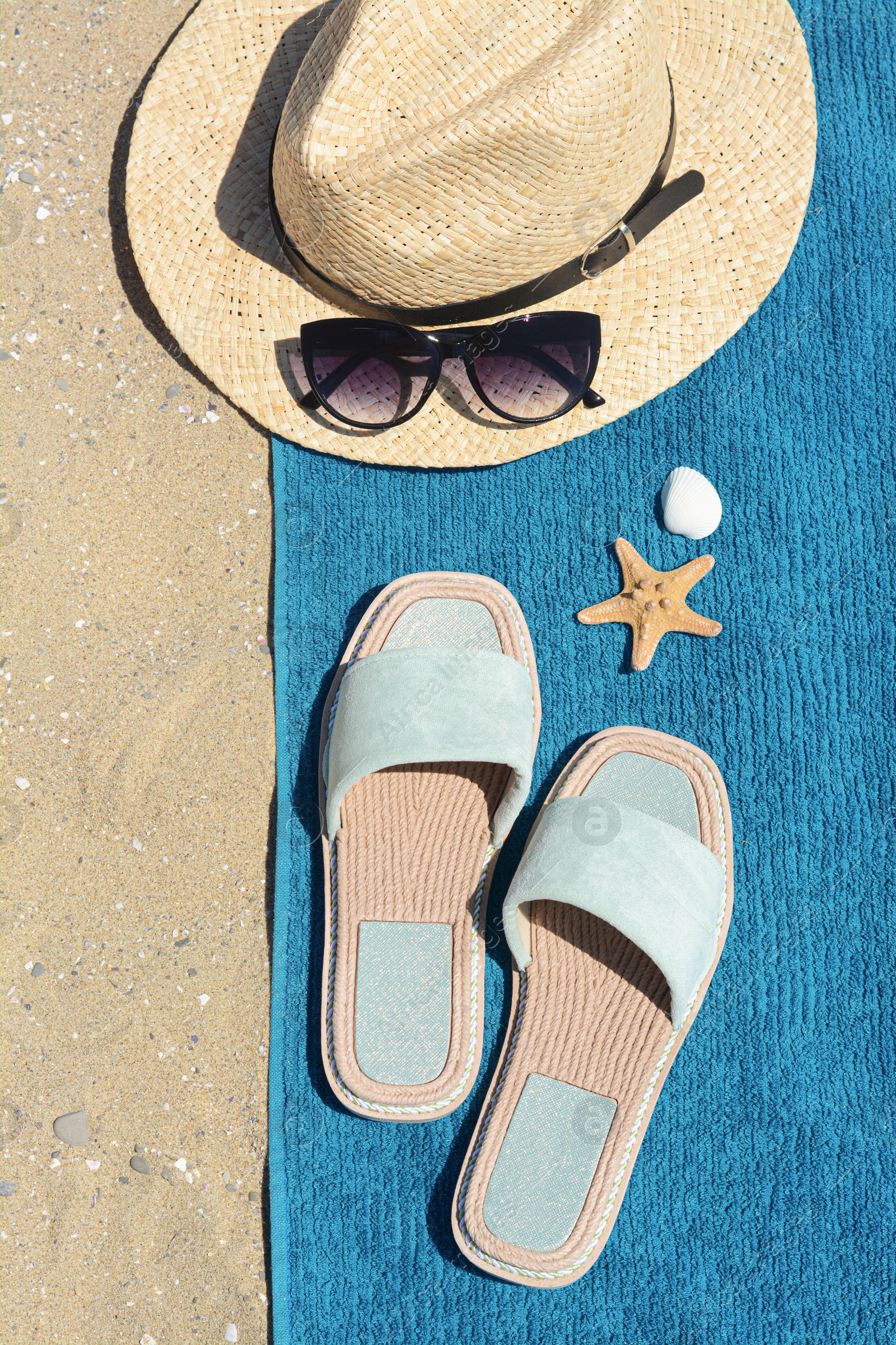 Photo of Stylish slippers, straw hat, sunglasses and blue towel on sand, flat lay. Beach accessories