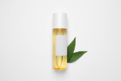 Photo of Bottle of cosmetic product and green leaves on white background, flat lay