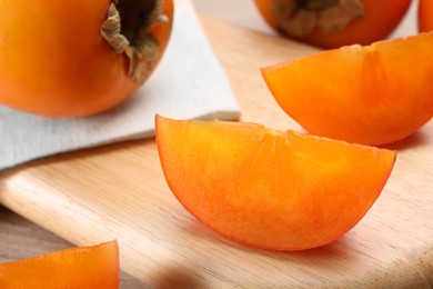 Photo of Delicious ripe persimmons on wooden board, closeup