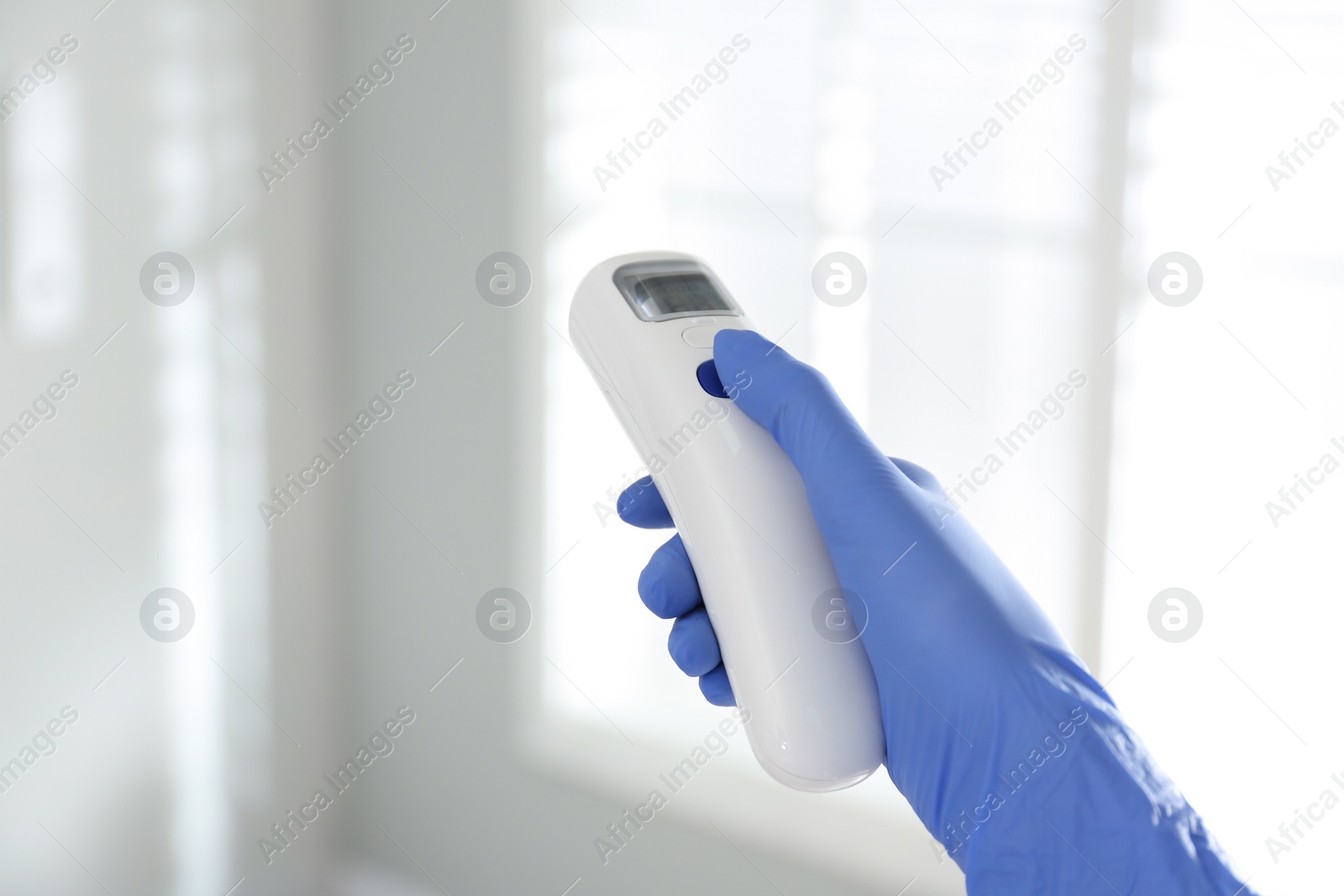 Photo of Doctor holding non contact infrared thermometer indoors, closeup. Measuring temperature