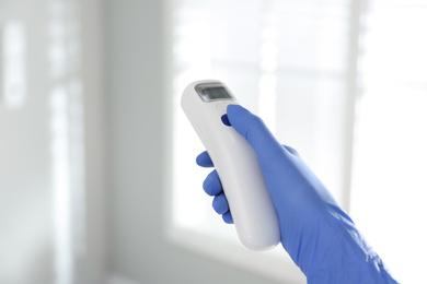 Photo of Doctor holding non contact infrared thermometer indoors, closeup. Measuring temperature