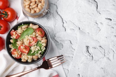 Photo of Delicious quinoa salad with tomatoes, beans and spinach leaves served on white textured table, flat lay. Space for text