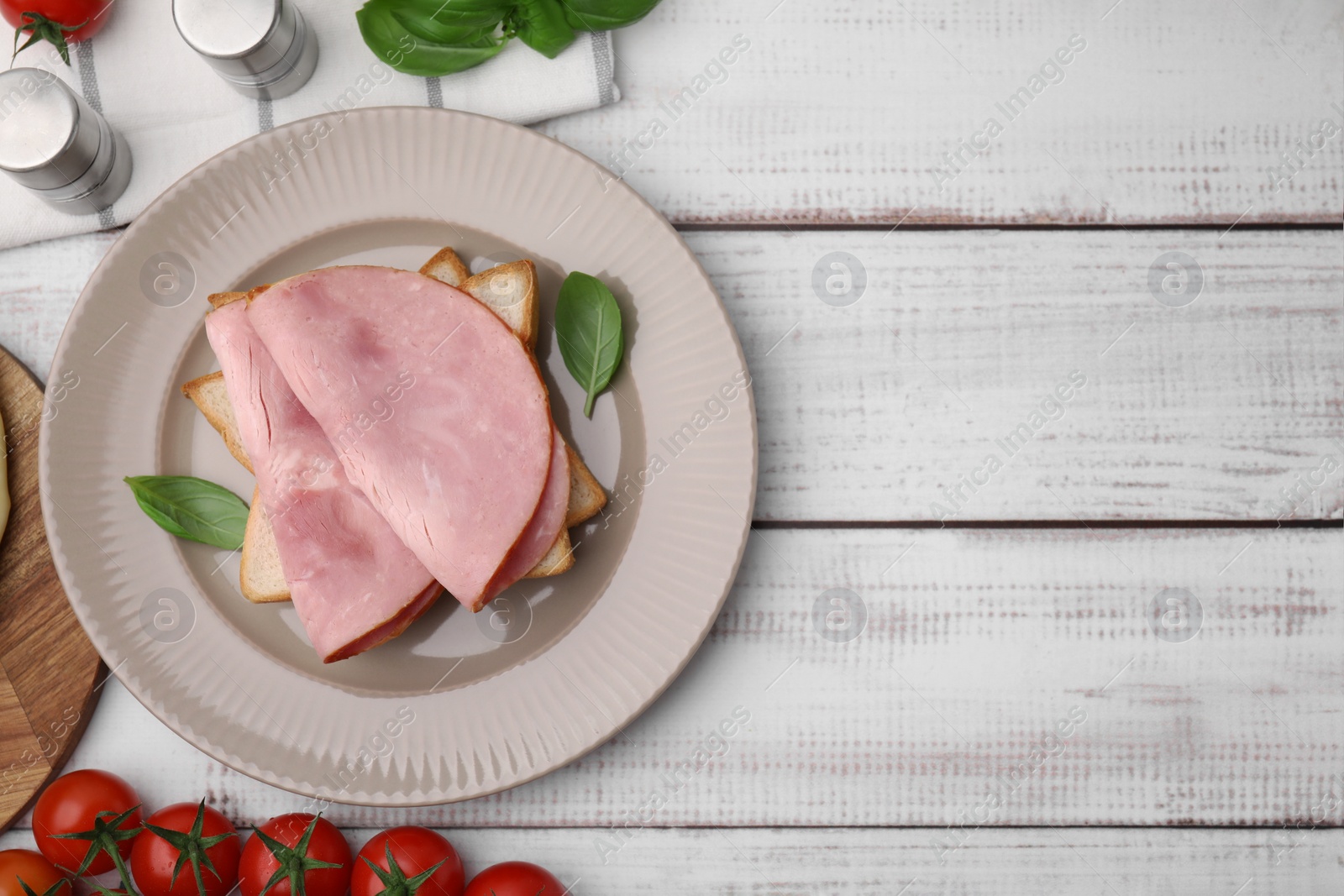 Photo of Delicious sandwich with ham, basil and tomatoes on white wooden table, flat lay. Space for text