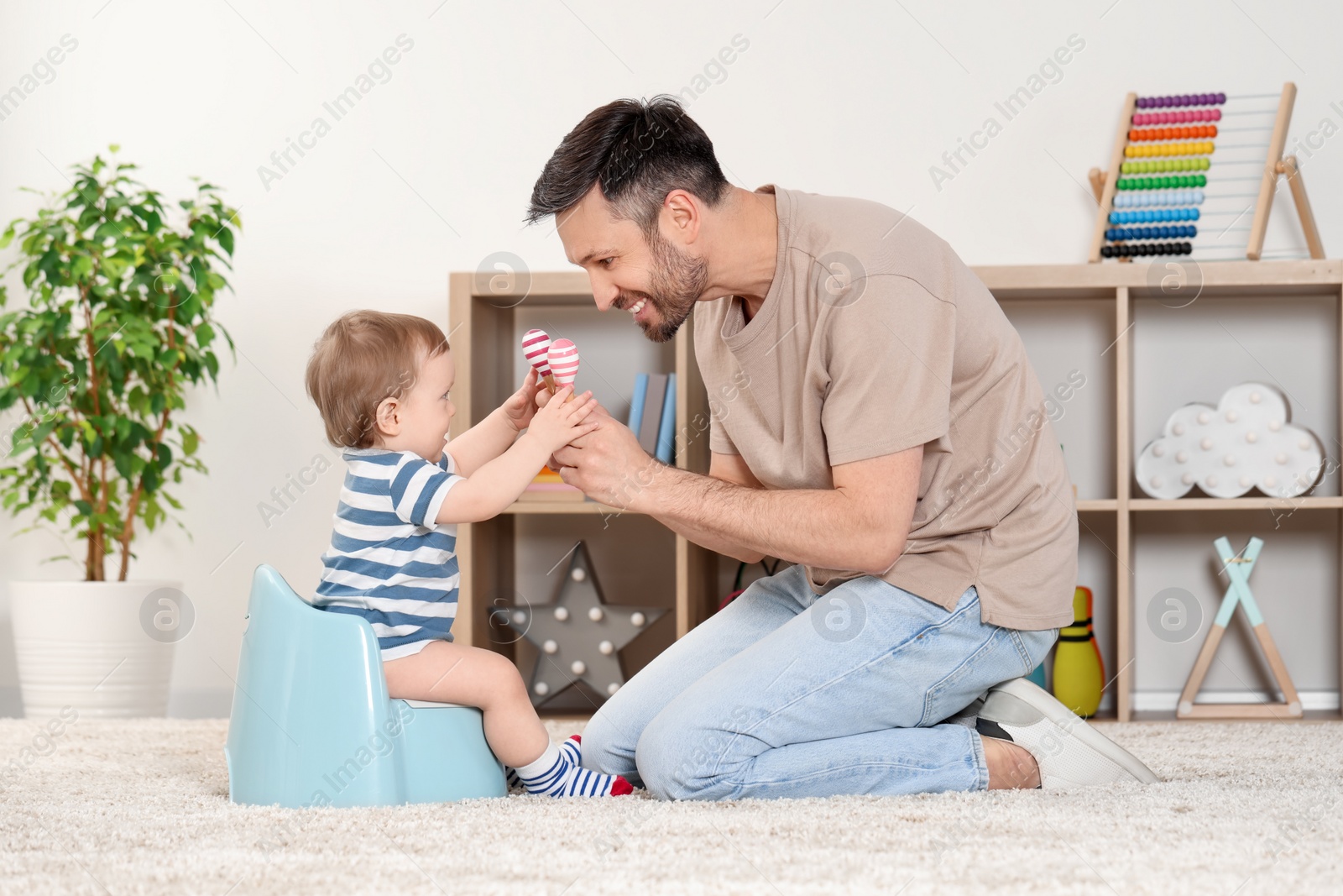 Photo of Father training his child to sit on baby potty indoors