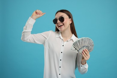 Photo of Happy woman with dollar banknotes on light blue background