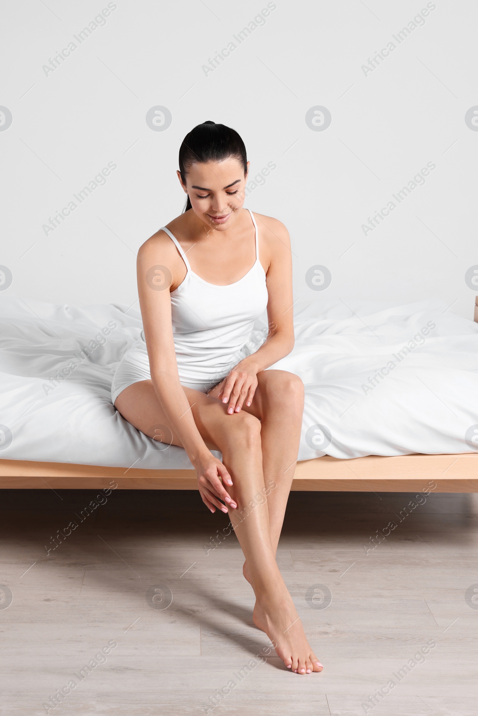 Photo of Young woman with beautiful smooth legs sitting on bed at home
