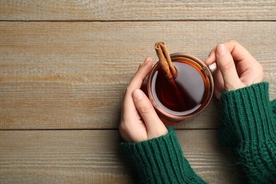 Woman holding cup of hot tea with aromatic cinnamon at wooden table, top view. Space for text