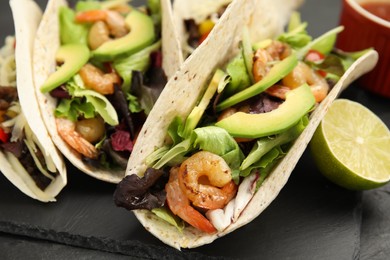 Photo of Delicious tacos with shrimps and avocado on black table, closeup