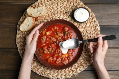 Woman with bowl of delicious stuffed pepper soup at wooden table, top view