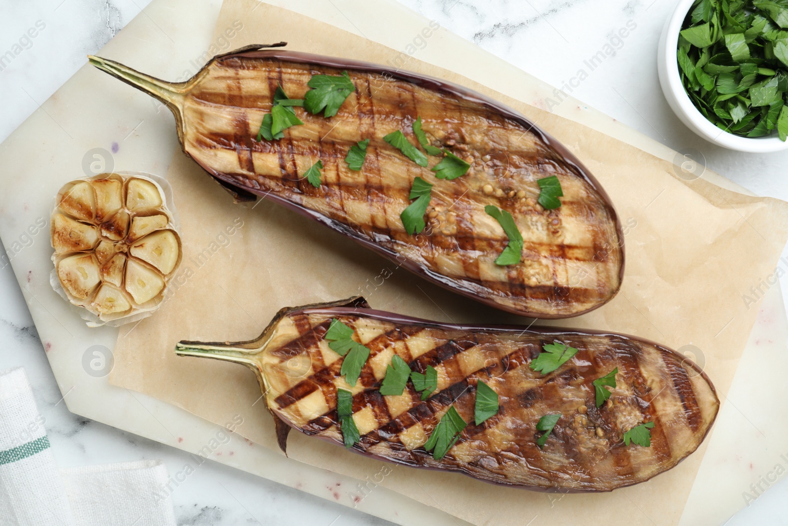 Photo of Delicious grilled eggplant halves with parsley on white marble table, flat lay