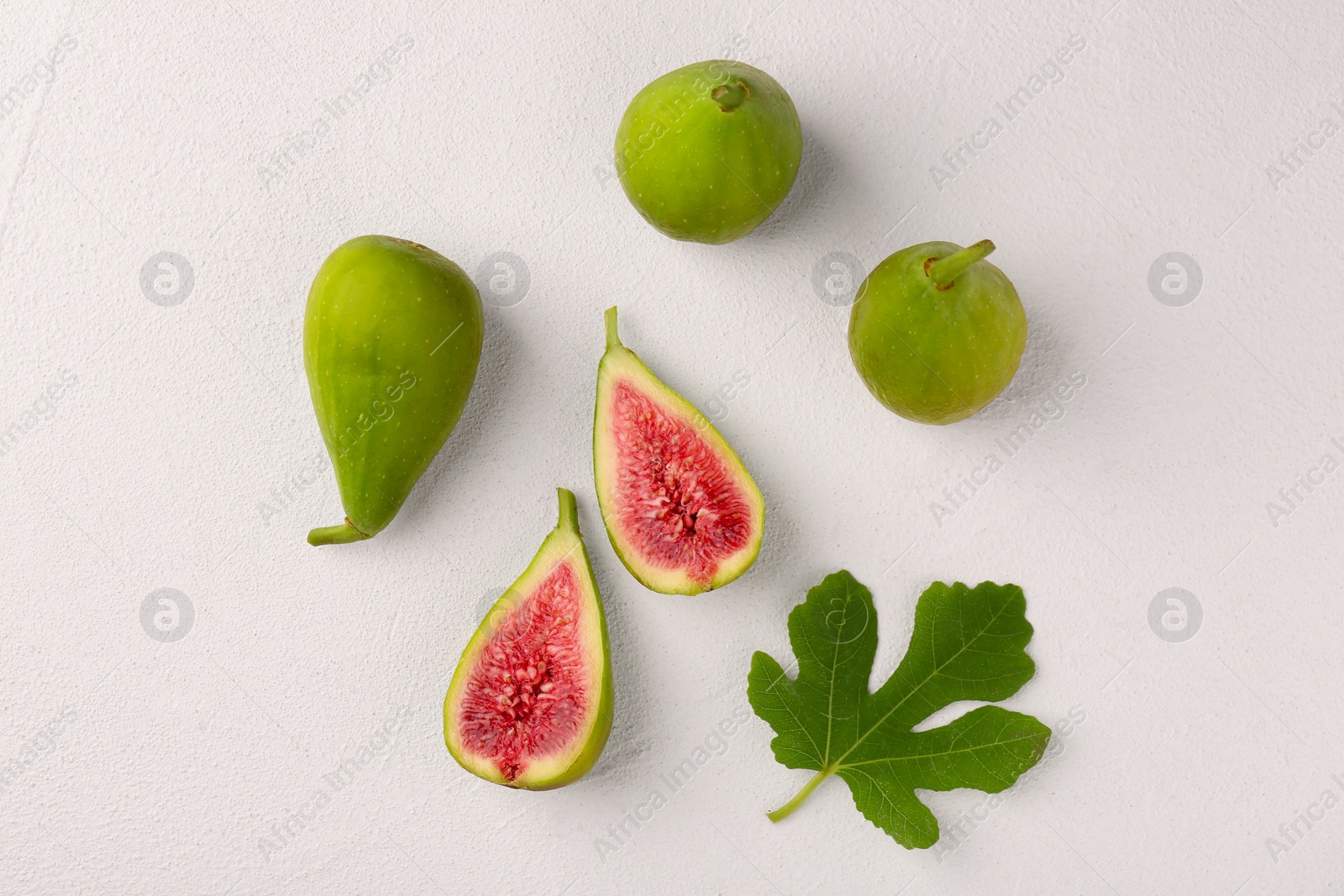 Photo of Cut and whole green figs with leaf on light table, flat lay