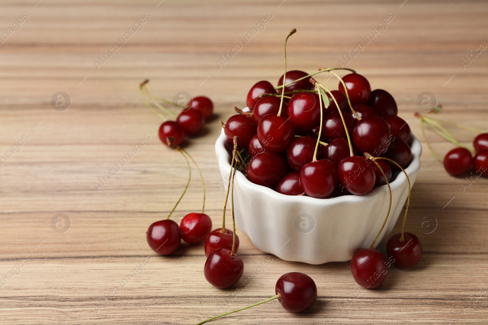 Photo of White bowl of delicious cherries on wooden table, space for text