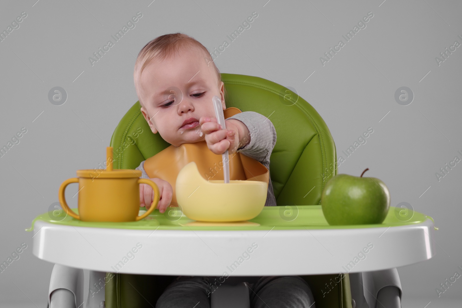 Photo of Cute little baby eating healthy food in high chair on gray background