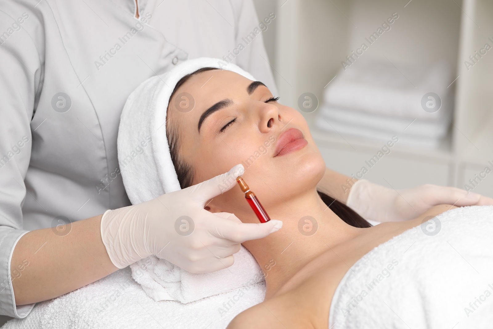 Photo of Professional cosmetologist holding skincare ampoule while working with client in clinic, closeup