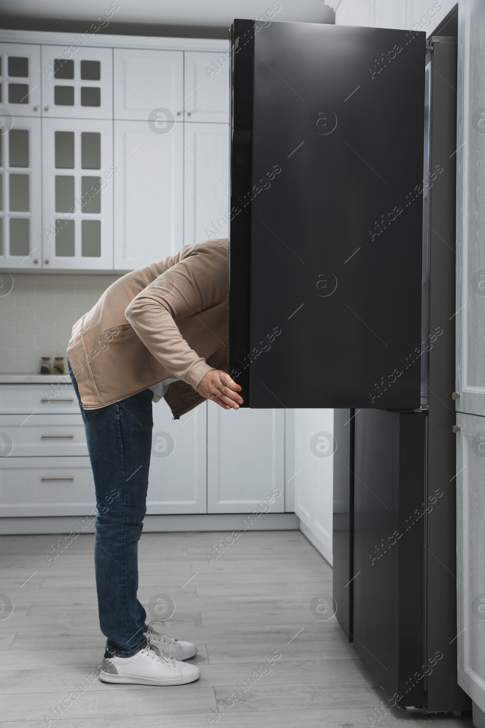 Photo of Young man looking into open refrigerator in kitchen